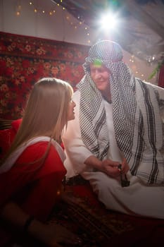 Portrait of young arabian muslim couple in traditional clothes in cozy red room. Fhoto shoot in easten style with male and female model like in harem with a sultan and an odalisque. Partial focus