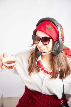 Portrait of young girl in a bright red scarf and large headphones with a microphone. A woman who is radio or television presenter with cap of tee. Funny female telecom operator. Freelancer at work