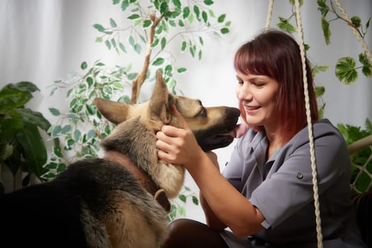 happy beautiful girl with cute big dog in the room full of flowers and plants. Adult middle aged woman with german shepherd. Friendship and love