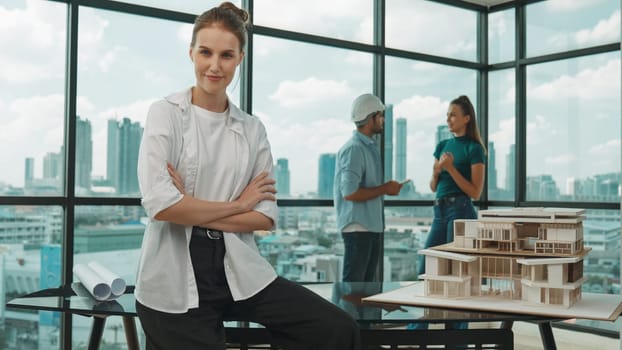 Young beautiful businesswoman sitting with arm folded while colleague discussion about house construction. Smart skilled architect engineer looking and smiling at camera with confident. Tracery