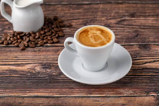 Espresso macchiato in white porcelain cup with milk and coffee beans on wooden table