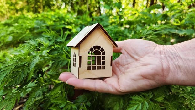 Small wooden toy house on palm of woman hand on natural background. symbol and concept of care of family and buying, selling, donating of eco friendly home. copy space. close-up. soft selective focus