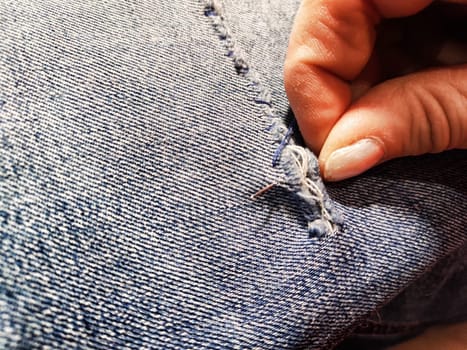 Woman repairing a pair of blue jeans. Fingers with a needle and torn jeans fabric. Sewing up a tear on blue fabric