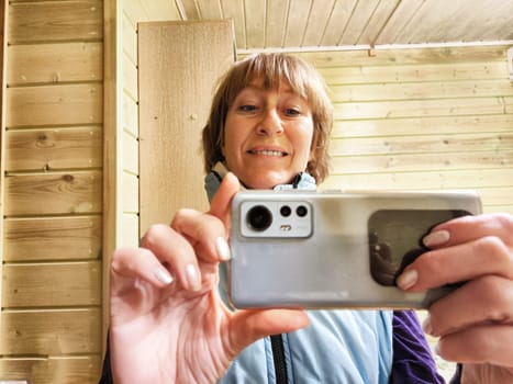 Middle-aged woman using smartphone for selfie and blogging. Female blogger poses in a photo. The girl admires herself in the mirror