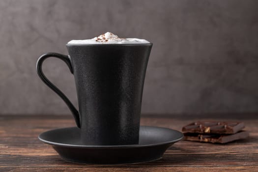 Hot chocolate in a black porcelain cup with a chocolate bar next to it