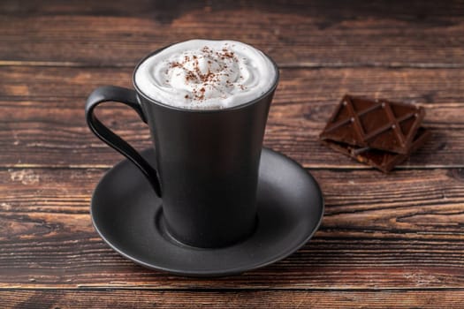 Hot chocolate in a black porcelain cup with a chocolate bar next to it