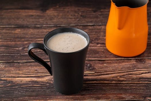 Milk with Turkish coffee in black cup on wooden table