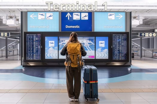 Young Asian woman in international airport looking at flight information board, checking her flight.