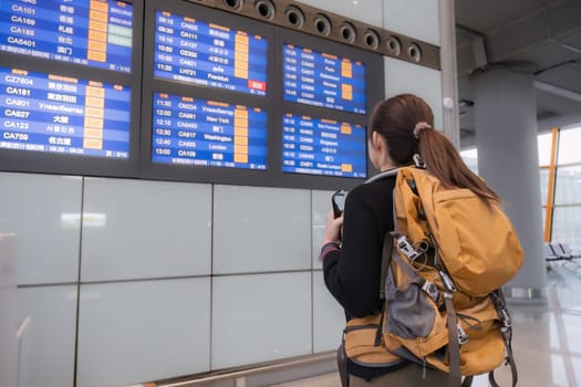 Young Asian woman in international airport looking at flight information board, checking her flight.