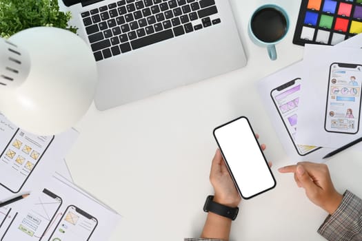 Young creative woman using mobile phone at desk with paper sketches for mobile interface.