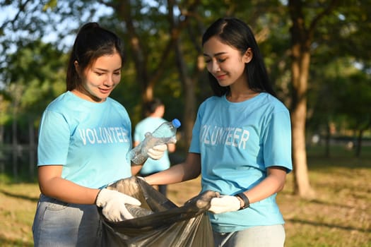 Image of volunteers picking up bottle into garbage bag while cleaning up nature in sunny day.