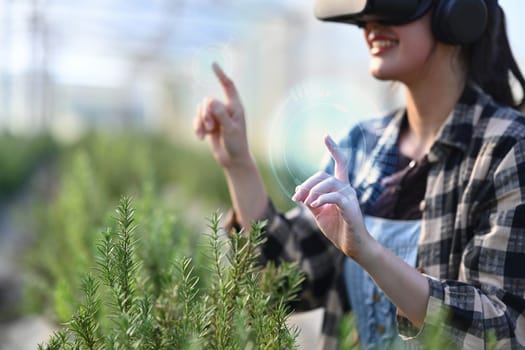 Smiling female farmer in VR glasses for digital management of greenhouse cultivation.