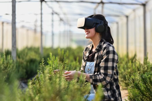 Cheerful female farmer with VR headset for analyzing and controlling plants quality in greenhouse.