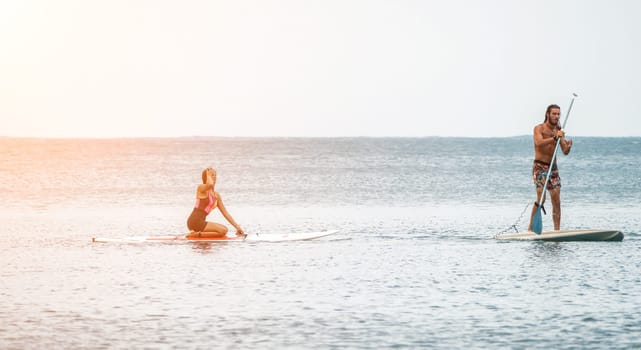 Sea woman and man on sup. Silhouette of happy young woman and man, surfing on SUP board, confident paddling through water surface. Idyllic sunset. Active lifestyle at sea or river