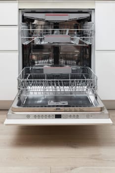 Modern built-in empty dishwasher with open door in the kitchen .