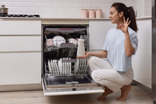 woman pours rinse aid into the dishwasher compartment in modern white kitchen