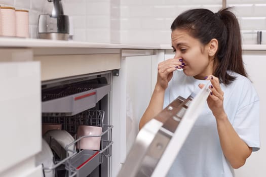 woman smells strange and terrible smell coming from dishwasher machine in kitchen