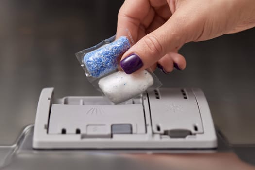 female hand puts dishwasher tablet into automatic dishwasher machine. Close-up