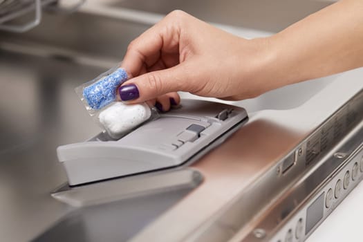 female hand puts dishwasher tablet into automatic dishwasher machine. Close-up