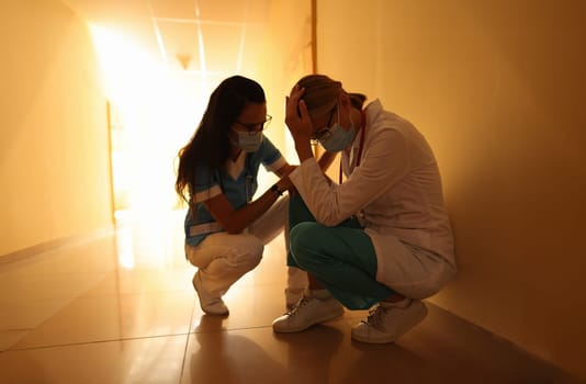 Nurse calms crying doctor in uniform and medical masks and sits in hospital corridor. Medical error concept.