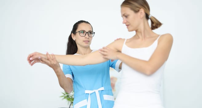 Woman doctor physiotherapist holds hand to woman patient in white clothes portrait. Diagnosis and treatment of rheumatic diseases of joints of plegia concept.