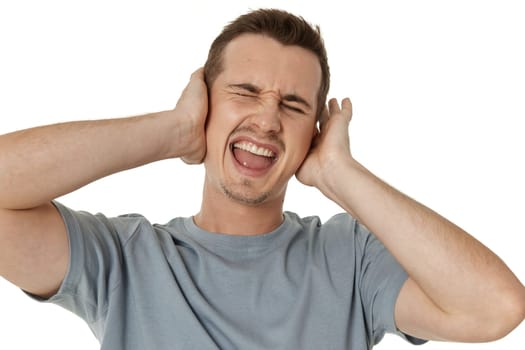 caucasian man in t-shirt covers ears with hands on white background