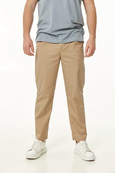 man wearing white sneakers and casual beige pants on studio background, front view