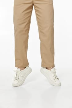 man wearing white sneakers and casual beige pants jumping on studio background, front view