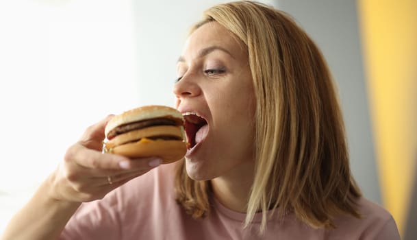 Young woman bites her mouth wide open hamburger. Unhealthy food fast food concept.