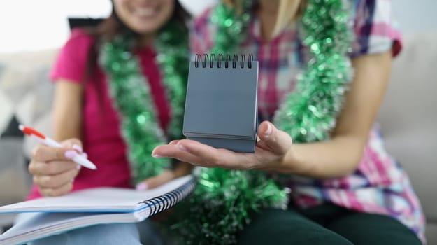 Woman make plan for new year with pen in notebook. Girlfriend hold calendar in her hand.