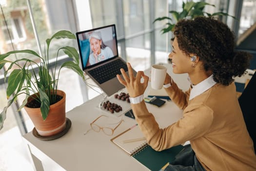 Female freelancer have video conference with client and showing sign Ok sitting in cozy coworking