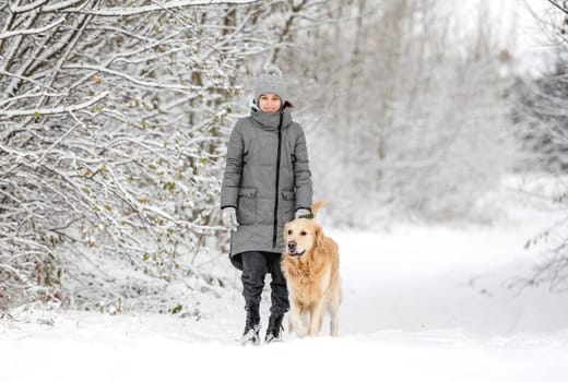 Teenage Girl With Golden Retriever Walks Through Snow-Covered Forest In Winter