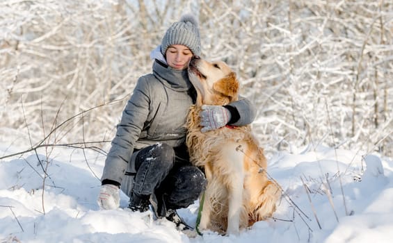 Teenage Girl And Golden Retriever Sit Together In Snow-Covered Forest During Winter