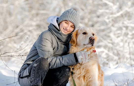 Teenage Girl And Golden Retriever Sit Together In Snow-Covered Forest During Winter