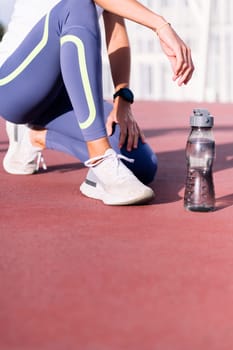 vertical photo of the legs of an unrecognizable female runner next to her water bottle, concept of healthy and active lifestyle, copy space for text