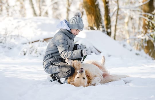 Teenage Girl Plays With Golden Retriever In Snowy Forest, Sitting With Dog