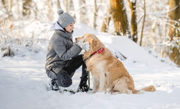 Teenage Girl And Golden Retriever Sit Together In Snow-Covered Forest During Winter