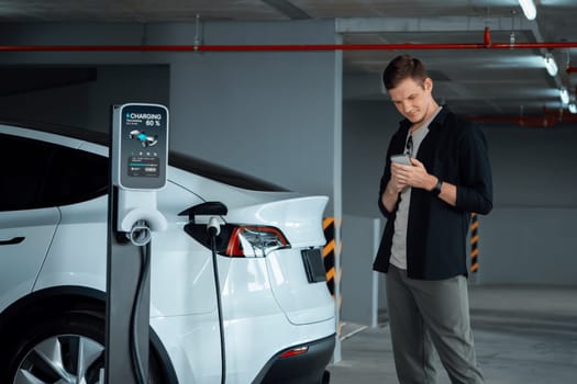 Young man travel with EV electric car to shopping center parking lot charging in downtown city showing urban sustainability lifestyle by green clean rechargeable energy of electric vehicle innards