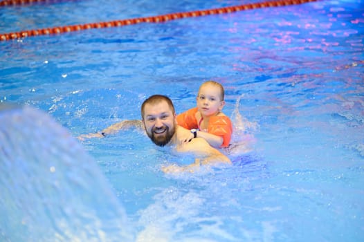 Dad and daughter are swimming in the pool with an inflatable. Healthy sports for the family.