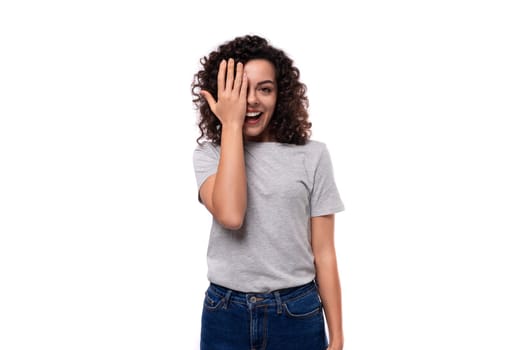 well-groomed european woman with natural black curly hair in a gray basic t-shirt on a white background.