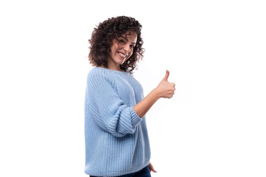 confident young brunette woman with curls dressed in a blue knitted sweater shows like.