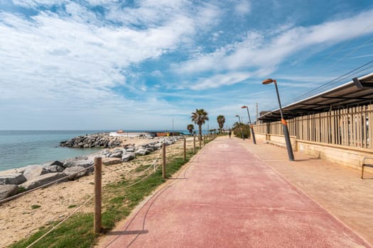 Railway station and road on waterfront by rocky beach in Vilassar de Mar. Tropical resort city with calm sea bay under picturesque sky