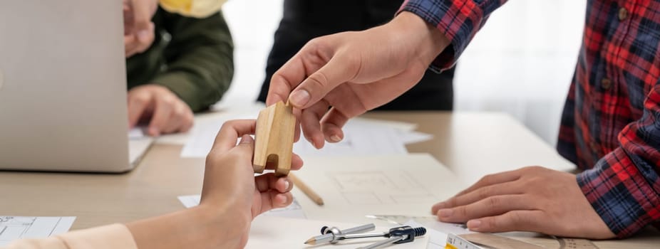 Professional architect team discussion about architectural project on meeting table with blueprint and wooden block scatter around at modern office. Closeup. Focus on hand. Delineation.