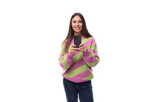 young slender caucasian woman with straight black hair dressed in a striped pink pullover communicates in social networks using a smartphone.