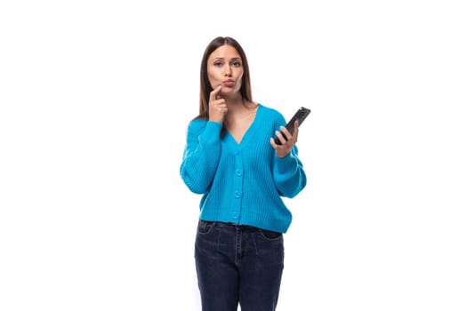 beautiful cute young woman dressed in a blue cardigan thinks holding a phone in her hand.