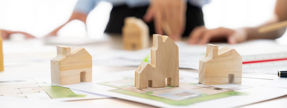 Professional architect engineer team discussion about architectural project on meeting table with wooden block and blueprint scatter around. Design and cooperate concept. Closeup. Delineation.