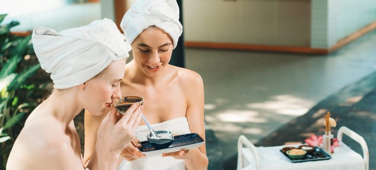 Couple of beautiful woman interested in homemade facial masks while sitting at spa salon. Attractive woman in white towel enjoy herbal masks with her friend surrounded by nature. Tranquility.