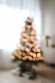 Cozy blur bokeh flat apartment room with Christmas Tree, gifts, presents, garlands, decorated interior of living room for New Year, lights glowing
