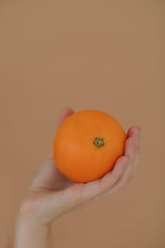 Hand holding orange. Tropical fruit in palm isolated on yellow background. Cropped view. Studio shot. Nutrition and vegetarian concept