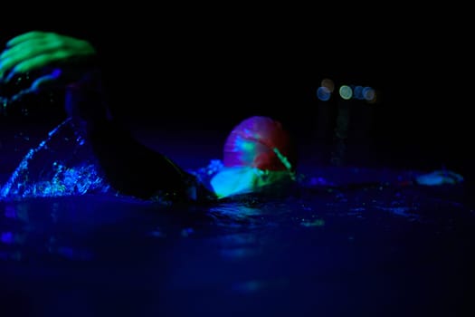 Real triathlete swimmer having a break during hard training at lake on dark night neon gel color lights